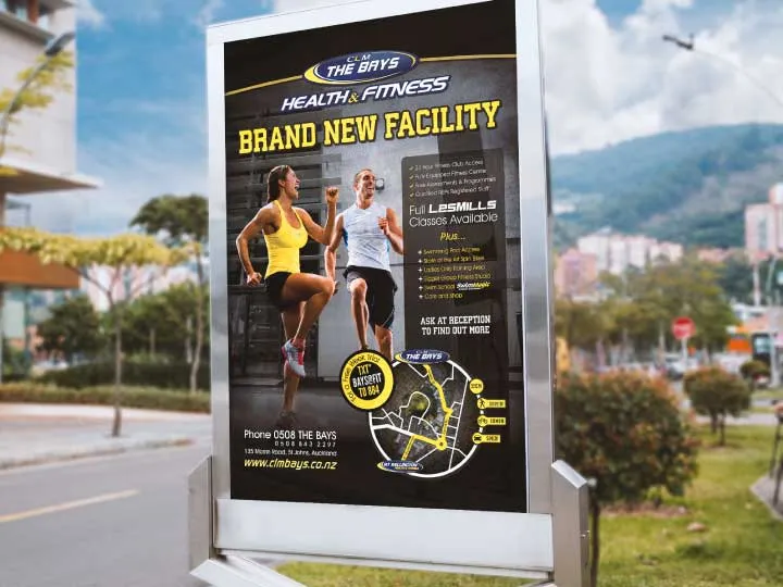 A street-side billboard showing a CLM The Bays Health and Fitness campaign poster for a brand-new facility.