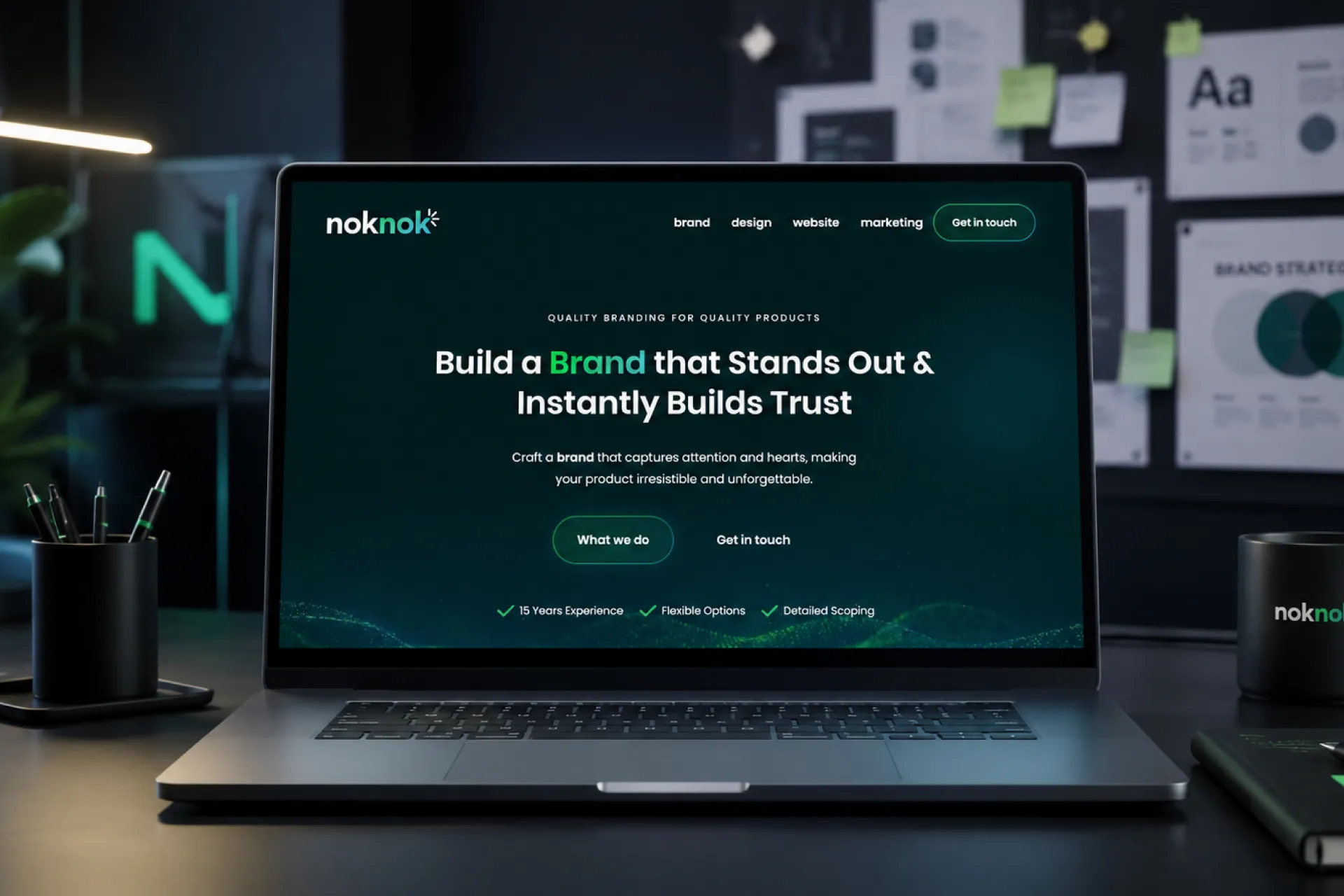 The Noknok Studios website shown on a laptop in the studio — 'Build a brand that stands out and instantly builds trust'.
