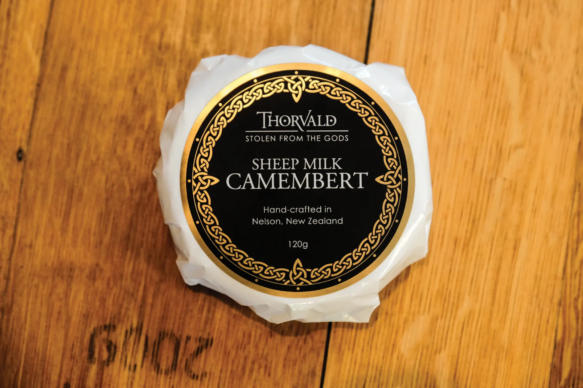 Thorvald sheep-milk camembert, with its black-and-gold Celtic label, on a wooden board.